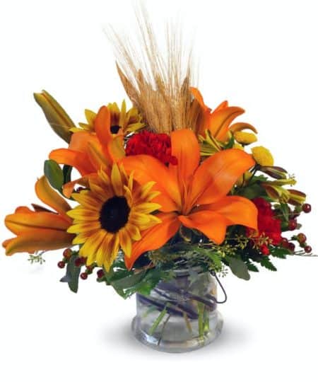 Gorgeous fall sunflowers, orange lilies, wheat and more fill this cube glass container. The perfect late-summer or autumn accent!