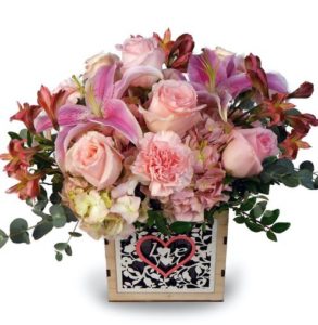 A pastel mix of fresh blooms dance above a detailed woodcut box that reads "Love You". Express how you feel with white lilies, lavender roses, pink carnations, hydrangea, and more!