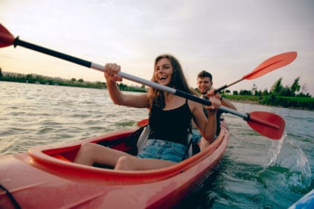 Confident young caucasian couple kayaking on river together with sunset in the backgrounds. Having fun in leisure activity. Romantic and happy woman and man on the kayak. Sport, relations concept.